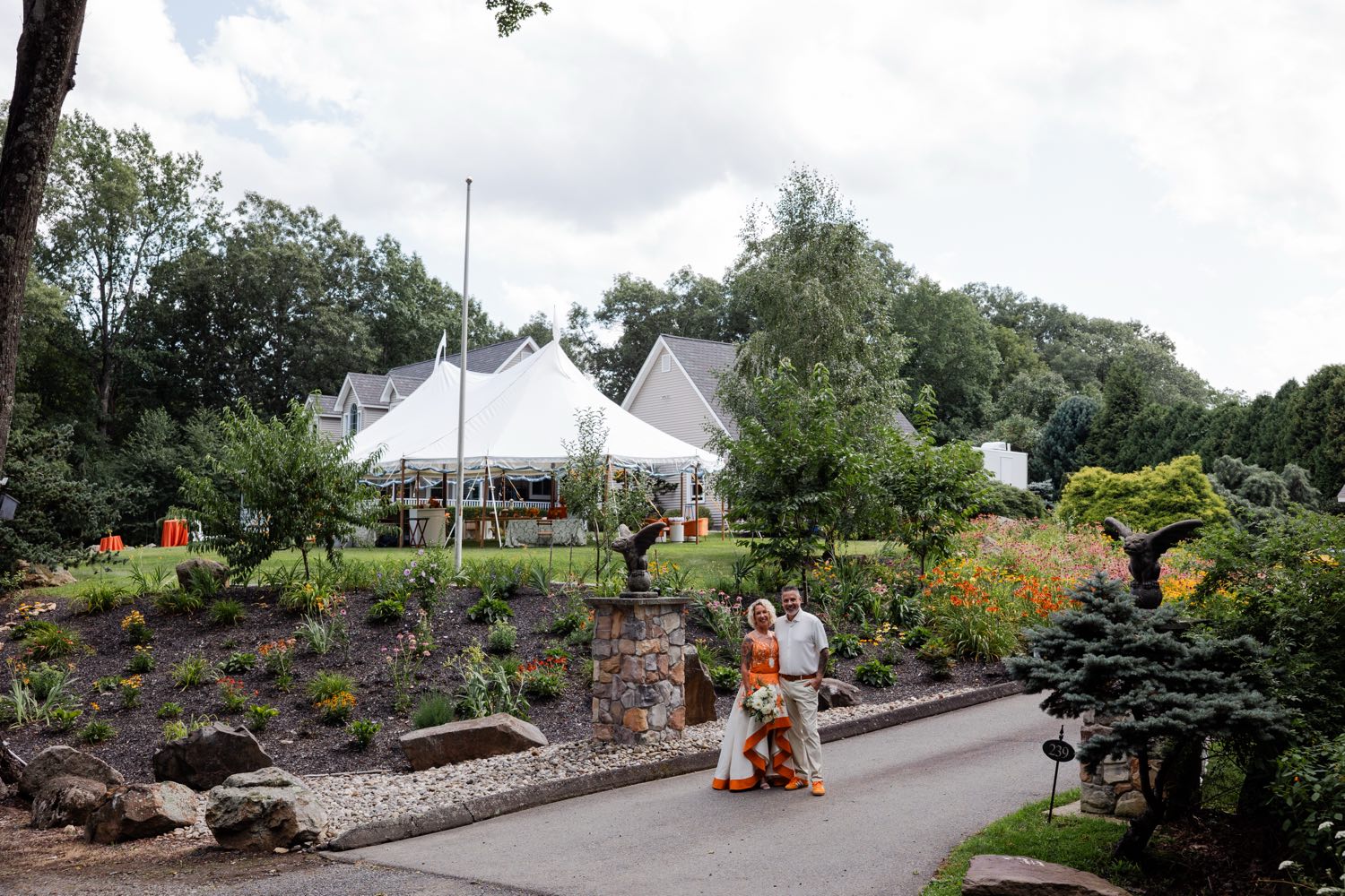 Jonathan and Lisa standing together at the end of the driveway at their wedding, with the white sailcloth reception tent, house, and flower gardens behind them