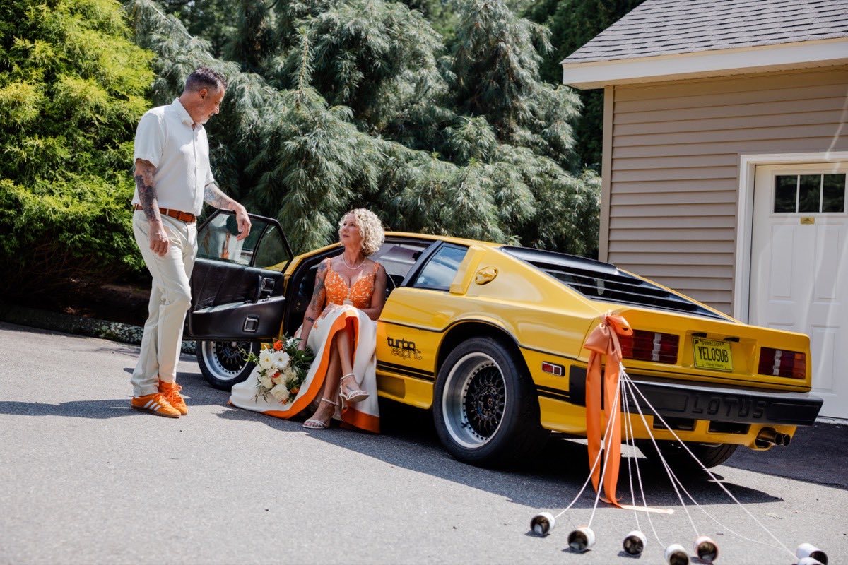 Jonathan and Lisa by their yellow Lotus Esprit getaway car after the ceremony, just-married cans trailing behind