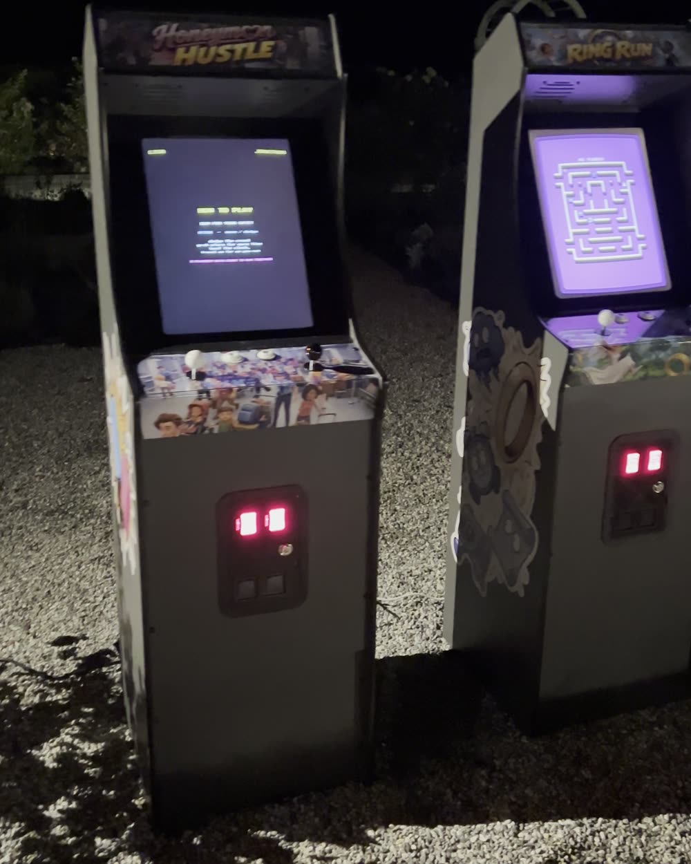 Both cabinets glowing after dark, their screens running the attract mode